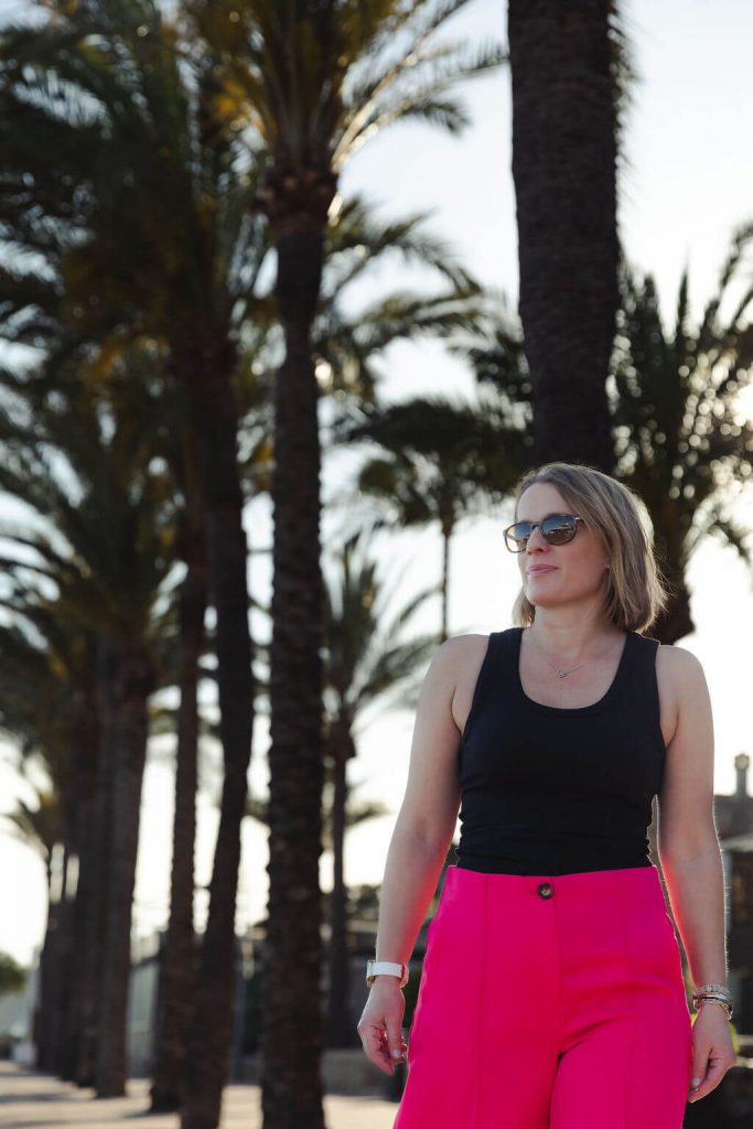 Clair of Chief Stew Shop wearing pink trousers and walking on the marina with palmtrees in the background during her personal branding shoot. 