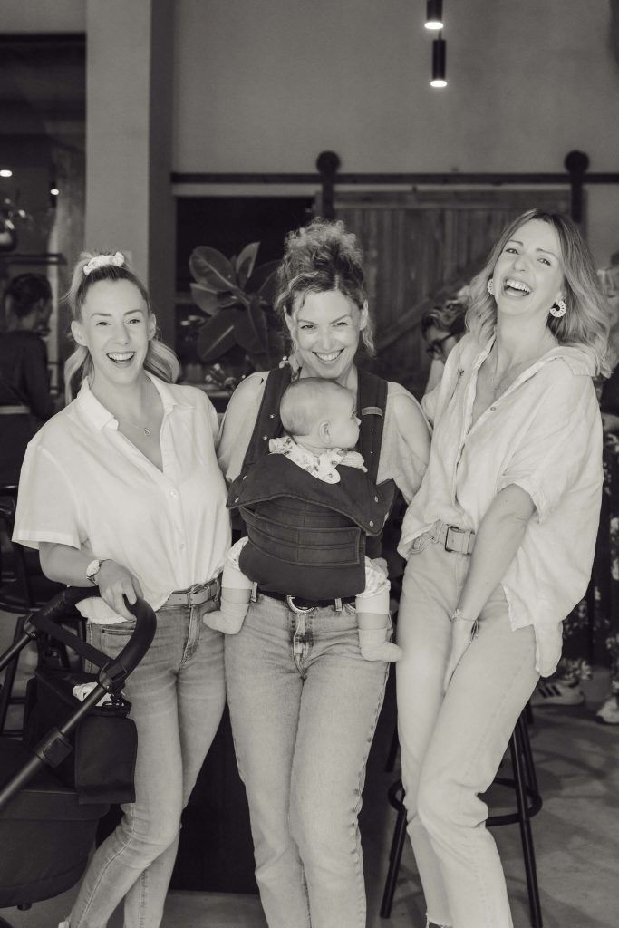 three women laughing at networking event in mallorca, one is carrying her baby 