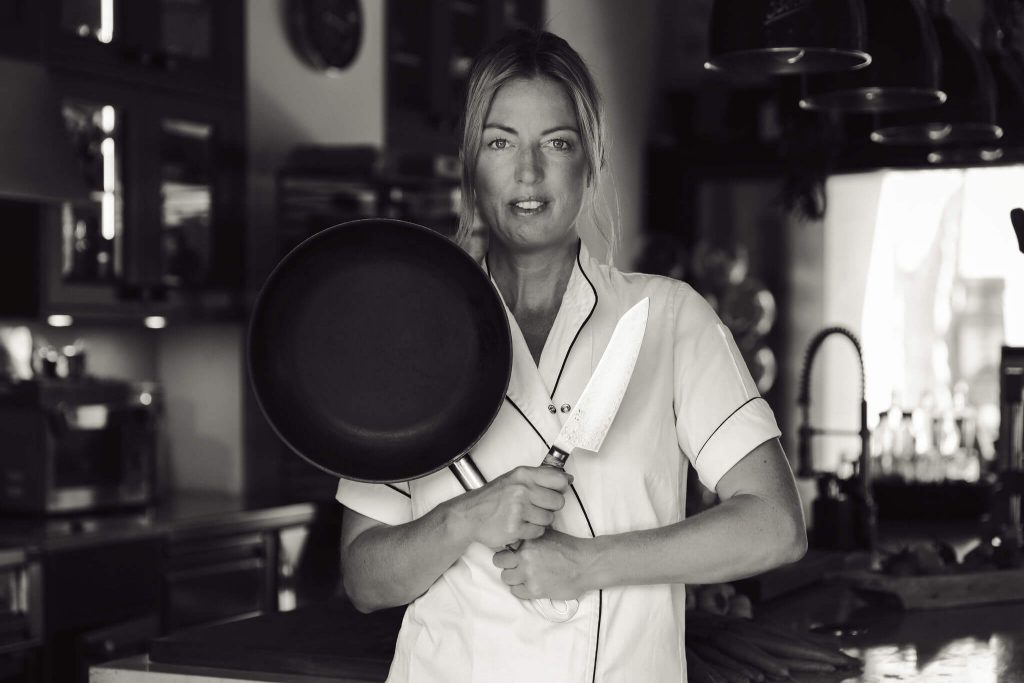 Private chef Ida in kitchen holding pan and knife for personal branding shoot in Mallorca