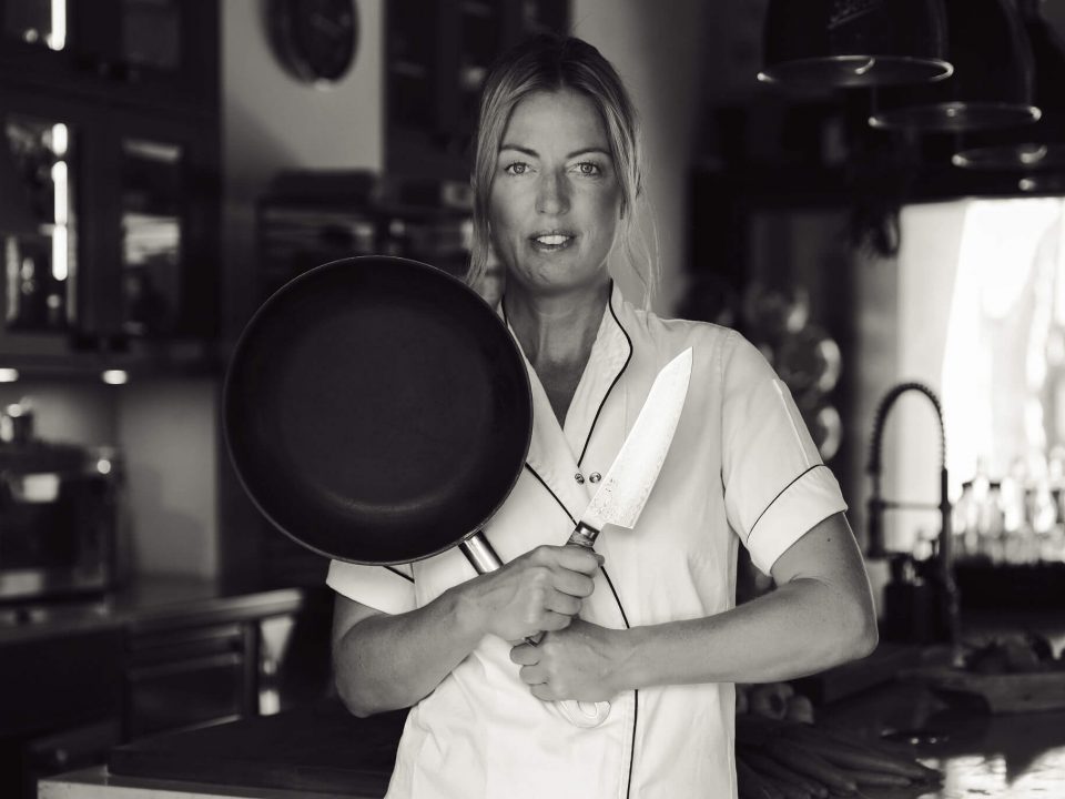 Private chef Ida in kitchen holding pan and knife for personal branding shoot in Mallorca